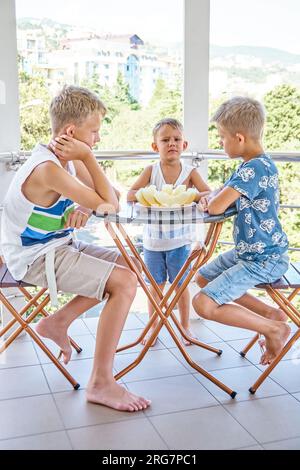 Kinder-, Kinder- und Vorschuljungen auf dem Hotelbalkon mit Scheiben frischer Melone. Brüder, die gemeinsam Obst essen wollen, im Strandresort Stockfoto