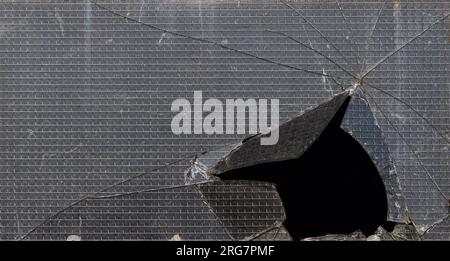 Gebrochenes verstärktes Glasfenster mit dunkelschwarzem Loch als Hintergrund Stockfoto