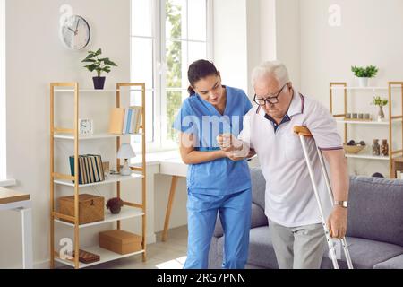 Krankenschwester hilft einem alten behinderten Mann mit Krücke zu gehen Stockfoto