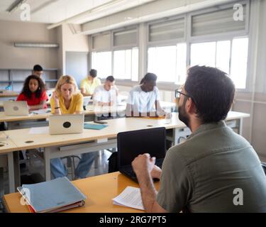 Männlicher Lehrer, der einer Klasse multiethnischer Schüler in einer Highschool die Lektion erklärt Stockfoto