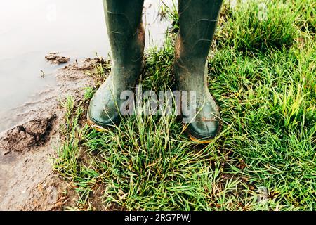 Bauer in Gummistiefeln, der nach heftigem Regensturm auf einer überfluteten Plantage auf dem Feld stand, selektiver Fokus Stockfoto