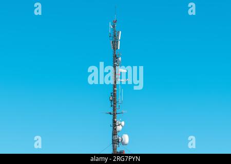Großer Telekommunikationsturm mit Antennen und Satellitenschüsseln, Repeater für Mobilfunksignale und 4G Sender und Sender gegen blauen Himmel Stockfoto