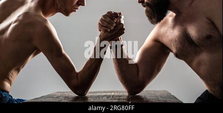 Arme ringen dünne Hand, großer starker Arm im Studio. Zwei Männerhände umklammten Arm Wrestling, stark und schwach, ungleiche Übereinstimmung. Stark muskulös bärtiger Mann Stockfoto