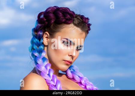 Ein bunter Känguru, geflochten in den Haaren. Hübsche Frau, farbenfrohes, violettes, ombernes Haar und professionelles Make-up. Zöpfe von Mädchen am Himmel. Leuchtendes Make-up Stockfoto