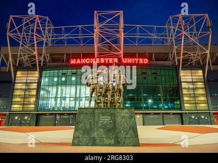 Manchester, Vereinigtes Königreich. 08.03.2023. Manchester Uniteds Old Trafford Stadium, Trinity Statue in der Dämmerung. 3. August 2023. Stockfoto