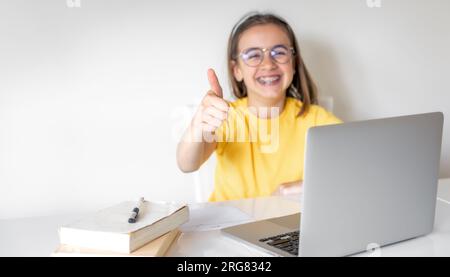 Süßes Schulmädchen mit einem Laptop, das zu Hause lernt, online lernt. Stockfoto