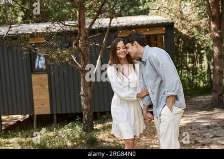 Positiv, Sommer, glücklicher Mann und wunderschöne Frau in einem Sonnenkleid, die Händchen in der Nähe des Ferienhauses hält Stockfoto