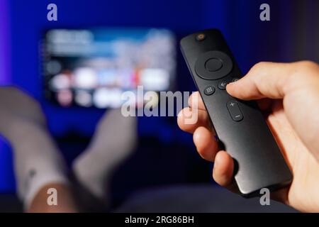 Hand mit tv-Fernbedienung. Mann, der zu Hause Inhalte von Streaming-Diensten ansieht Stockfoto