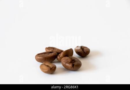 Dunkle Kaffeebohnen. Eine kleine Gruppe dunkler Kaffeebohnen auf der rechten Seite, isoliert auf weißem Hintergrund. Nahaufnahme. Selektiver Fokus. Stockfoto
