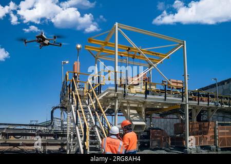 Drohnenbediener mit Fernbedienung für eine thermische UAV-Kamera, Vermessung einer Baustelle, in einem Industriegebiet, Drohneninspektion junger Bergbauarbeiter Stockfoto