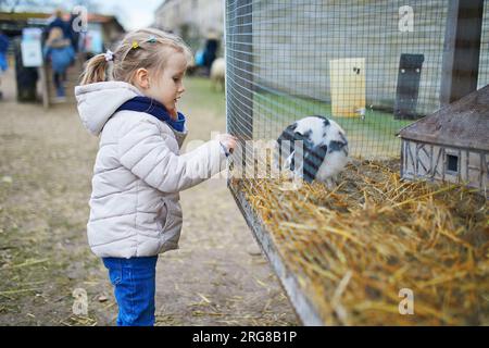 Ein bezauberndes kleines Mädchen, das auf dem Bauernhof mit Kaninchen spielt. Kind, das sich mit Tieren vertraut macht. Landwirtschaft und Gartenarbeit für Kleinkinder. Outdoor-Aktivitäten Stockfoto