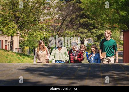 Eine Gruppe verschiedener Teenager, die Rucksäcke und Notizbücher tragen, interagieren und unterhalten sich, während sie die Parktreppe hinaufsteigen, die von der Hüfte nach oben sichtbar ist. Großzügige Kopie Stockfoto