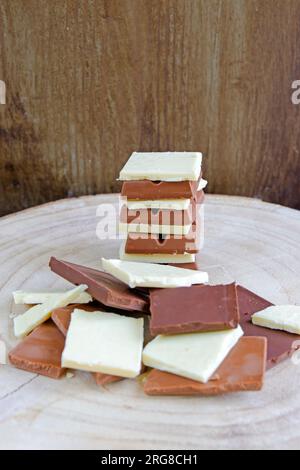 Weiße, Milch- und dunkle Schokoladenstücke bilden einen Stapel auf einem Holzboden. Vertikaler Schuss. Stockfoto