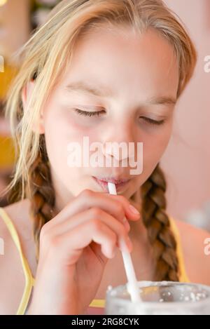 Ein hübsches Mädchen, elf Jahre alt, das Erdbeermilchshake durch einen Strohhalm trinkt, in einem Café. Portrait des glücklichen Mädchens, das einen Cocktail trinkt Stockfoto