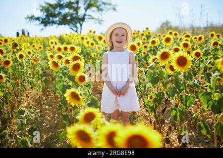 Bezauberndes 4-jähriges Mädchen in weißem Kleid und Strohhut auf einem Feld mit Sonnenblumen in der Provence, Frankreich Stockfoto