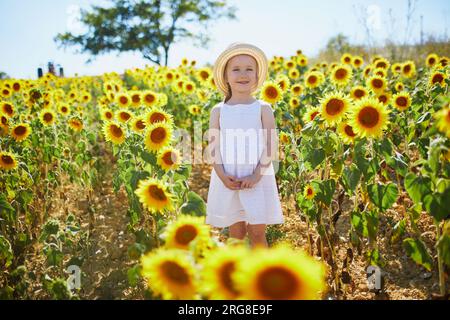 Bezauberndes 4-jähriges Mädchen in weißem Kleid und Strohhut auf einem Feld mit Sonnenblumen in der Provence, Frankreich Stockfoto