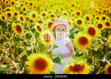 Bezauberndes 4-jähriges Mädchen in weißem Kleid und Strohhut auf einem Feld mit Sonnenblumen in der Provence, Frankreich Stockfoto