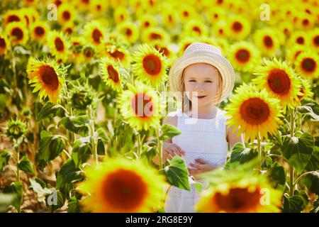 Bezauberndes 4-jähriges Mädchen in weißem Kleid und Strohhut auf einem Feld mit Sonnenblumen in der Provence, Frankreich Stockfoto