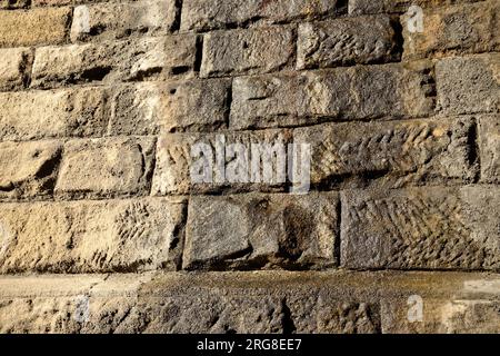 Eine strukturierte Oberfläche aus Granitblöcken, die eine Wand bilden. Etwas feuchtes Oberflächenwasser. Vielleicht ein Hintergrundbild. Stockfoto