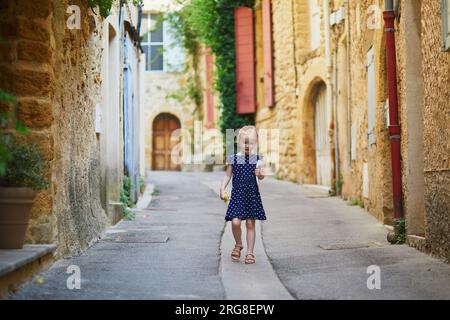 Bezauberndes Vorschulmädchen, das auf einer Straße des mittelalterlichen Dorfes Lourmarin in der Provence, Südfrankreich, spaziert Stockfoto