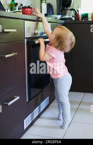 Ein kleines Mädchen, das versucht, in der Küche eine Schüssel mit Kirschen zu erreichen. Kleines Kind zu Hause Stockfoto