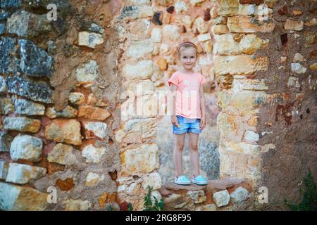 Fröhliches Vorschulmädchen, das Spaß an der Backsteinmauer in Roussillon, Provence, Südfrankreich hat Stockfoto
