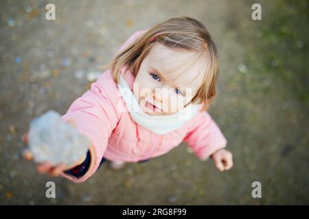 Ein bezauberndes kleines Mädchen, das im Frühling oder Herbst Steine im Park sammelt. Aktivitäten im Freien für Kinder Stockfoto