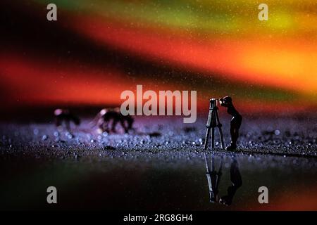 Miniaturfotograf in Aktion mit simuliertem aurora-Hintergrund. Aurora (PL: Aurorae oder auroras), auch bekannt als Polarlichter, nördlicher li Stockfoto