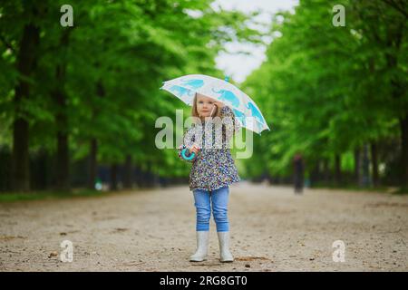 Ein Kind trägt Regenstiefel mit Regenschirm an einem Herbsttag. Ein bezauberndes Kleinkind, das an einem Regentag Spaß hat. Herbstaktivitäten im Freien für Kinder Stockfoto