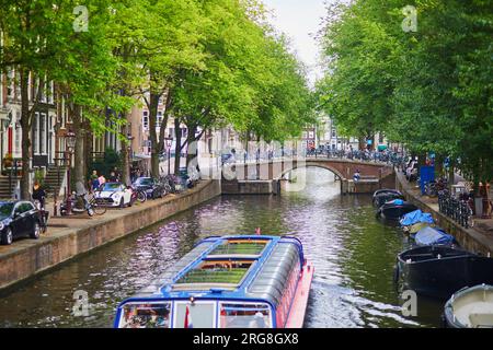 AMSTERDAM, NIEDERLANDE - 18. AUGUST 2022: Die Menschen genießen einen schönen Frühlingstag in Amsterdam mit seinen Kanälen, Brücken und Booten Stockfoto