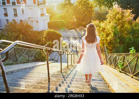 Wunderschöne junge Frau in weißem Kleid, die am frühen Morgen auf dem berühmten Montmartre-Hügel in Paris, Frankreich, spaziert Stockfoto