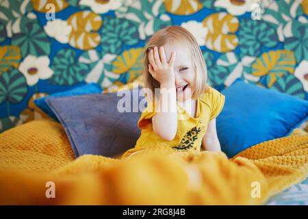 Ein bezauberndes, verspieltes kleines Mädchen, das auf dem Bett in einem schön eingerichteten Schlafzimmer sitzt Stockfoto