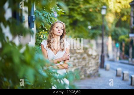 Wunderschöne junge Frau in weißem Kleid, die sich am frühen Morgen an die Wand auf dem Montmartre-Hügel in Paris, Frankreich, lehnt Stockfoto