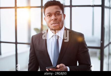 Ein junger afroamerikanischer Geschäftsmann hielt sein Smartphone in den Händen, tippte Nachrichten, chatte mit Freunden in sozialen Netzwerken Stockfoto