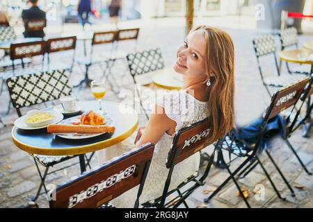 Eine fröhliche junge Frau frühstückt oder brunch im traditionellen französischen Café auf Montmartre in Paris, Frankreich Stockfoto