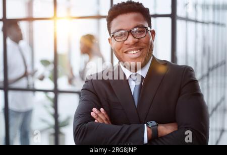 Attraktiver Kerl mit einem charmanten Lächeln und einer Brille mit nach vorne gefalteten Armen Stockfoto