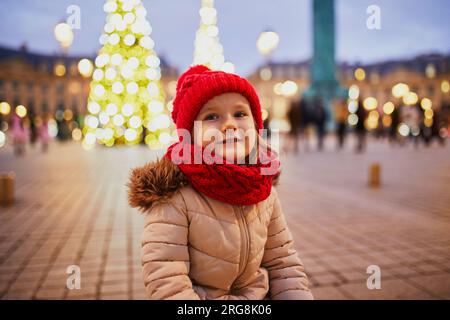 Fröhliches Vorschulmädchen mit rotem Hut auf dem Place Vendome, dekoriert zu Weihnachten in Paris, Frankreich Stockfoto