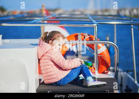 Süßes Vorschulmädchen, das auf dem Deck einer Fähre sitzt und von Marken nach Volendam, Nordholland, Niederlande, fährt Stockfoto