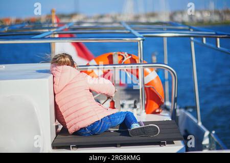 Süßes Vorschulmädchen, das auf dem Deck einer Fähre sitzt und von Marken nach Volendam, Nordholland, Niederlande, fährt Stockfoto