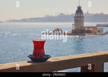 Türkisches Glas in Form einer Tulpe gefüllt mit heißem schwarzem Tee mit Blick auf den Maiden's Tower im Uskudar-Viertel auf der asiatischen Seite von Istanbul, Türkei Stockfoto