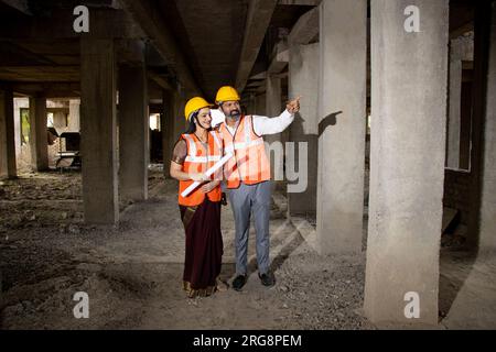 Zwei indische Bauingenieure oder Architekten mit Helm und Weste mit Papierkram und Baustellenplan, Rea Stockfoto