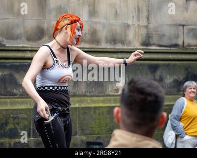 Eine Straßenkünstlerin führt während des Fringe Festivals am 2023. August auf der Royal Mile in Edinburgh ihre „blutige“ Tat auf, bei der sie Nägel in die Nase hämmert. Stockfoto