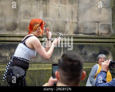 Eine Straßenkünstlerin führt während des Fringe Festivals am 2023. August auf der Royal Mile in Edinburgh ihre „blutige“ Tat auf, bei der sie Nägel in die Nase hämmert. Stockfoto