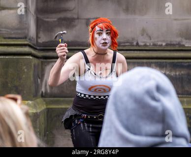 Eine Straßenkünstlerin führt während des Fringe Festivals am 2023. August auf der Royal Mile in Edinburgh ihre „blutige“ Tat auf, bei der sie Nägel in die Nase hämmert. Stockfoto