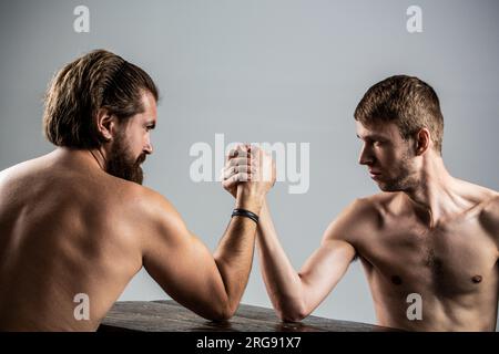 Arme ringen dünne Hand, großer starker Arm im Studio. Zwei Männerhände umklammten Arm Wrestling, stark und schwach, ungleiche Übereinstimmung. Armdrücken. Stark Stockfoto