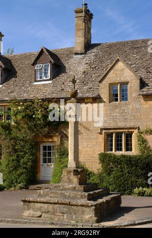 Blick auf eine Reihe von Cottages in Stanton Village, in der Nähe des Broadway, in den Cotswolds, Gloucestershire. Im Vordergrund befindet sich eine Sonnenuhr auf einem mittelalterlichen Kreuz. Stockfoto