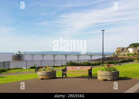 Weiter Blick auf den Pier im Badeort Clevedon in der Grafschaft Avon, mit einer Bank und Blumenwannen im Vordergrund. Der Pier wurde 1869 eröffnet. Seitdem wurden zahlreiche Reparatur- und Restaurierungsarbeiten durchgeführt, und der Pier ist nun ein Gebäude der Kategorie I. Stockfoto