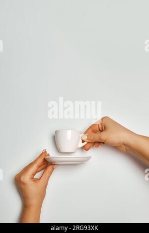 Weibliche Hände halten eine weiße Kaffeetasse und Untertasse auf weißem Hintergrund, Konzept Stockfoto