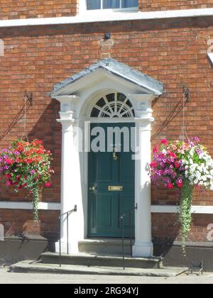 Eine Eingangstür in der High Street, Pershore, Worcestershire, mit bunten Hängekörben auf beiden Seiten. Stockfoto