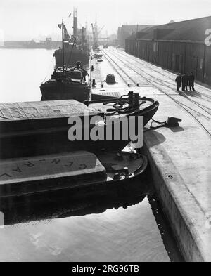 Stimmungsvolle Hafenlandschaft mit Schiffen und Kranen auf der Themse, Hafen von London, mit einer Gruppe von vier Männern, die auf der rechten Seite spazieren gehen. Stockfoto